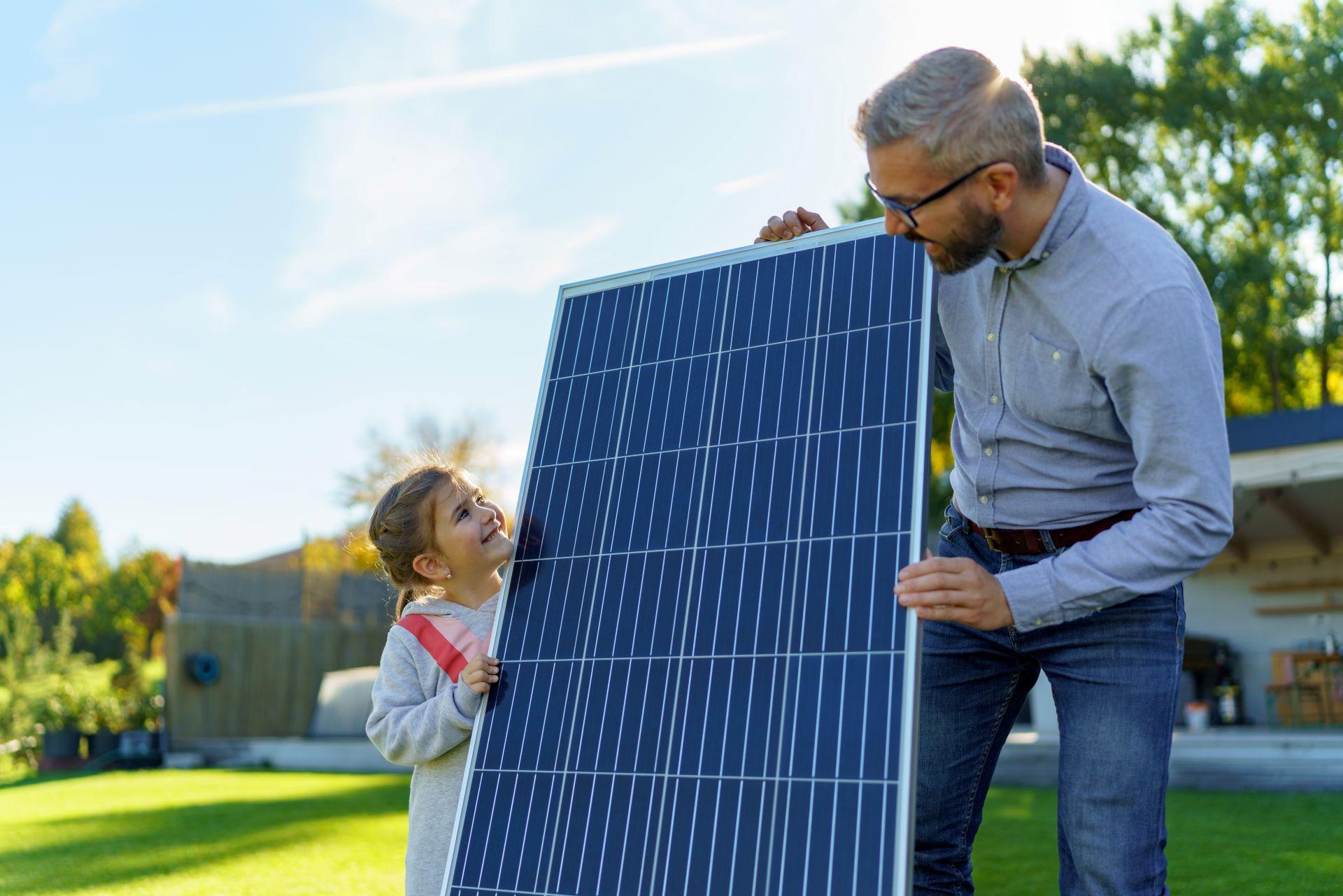 Vater und Tochter halten zusammen ein Solarpanel im Garten. Das Bild zeigt die Freude an erneuerbaren Energien und den Einsatz von Solarenergie im eigenen Zuhause.